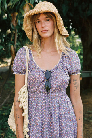 Woman wearing a purple floral dress and straw hat outdoors