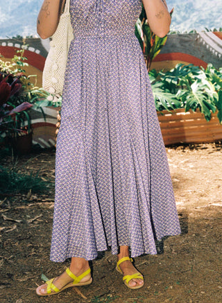 Person wearing a long purple floral dress with yellow sandals in an outdoor setting.