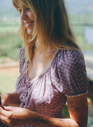 Woman wearing a purple patterned dress with a blurred natural background