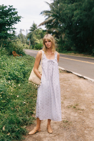 Woman in a floral dress standing on a path with greenery and a road in the background