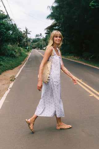 Woman in a white dress with a pattern walking on a road surrounded by greenery.