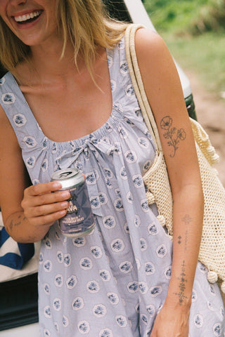 Woman in a floral dress holding a can, standing outdoors with a blurred background