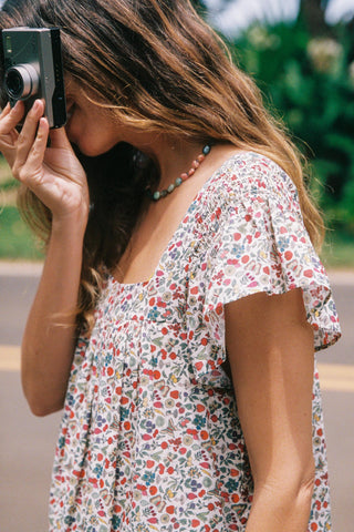 Woman in a floral dress holding a camera outdoors