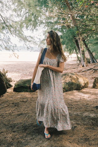 Woman in a floral dress standing by a lake with trees in the background