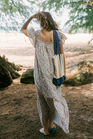 Woman in a floral dress with a blue and white bag walking through a forest.