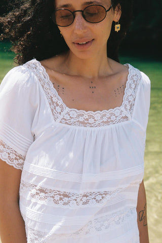 Woman wearing a white lace top with a blurred natural background