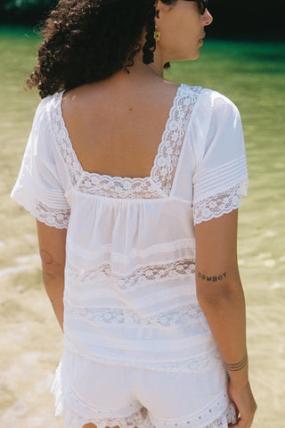 Woman wearing a white lace dress standing on a beach.