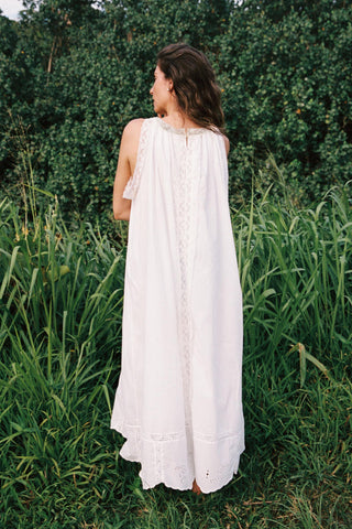 Woman in a white dress standing in a grassy field with greenery in the background
