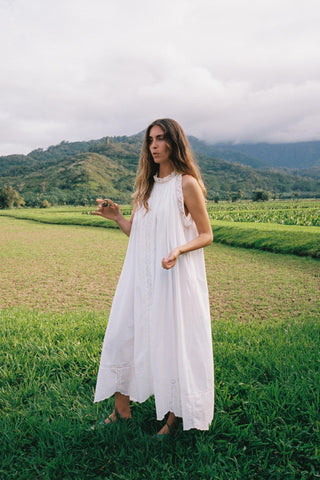 Woman in a white dress standing in a grassy field with mountains in the background
