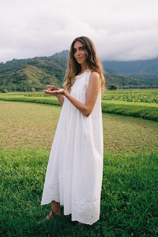 Woman in a white dress standing in a field with mountains in the background