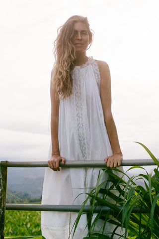 Woman in a white dress standing outdoors with greenery and a mountainous background
