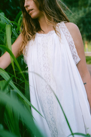 Woman in a white lace dress standing among tall green grass