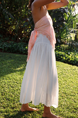 Person wearing a light pink top and white skirt standing on grass with plants in the background