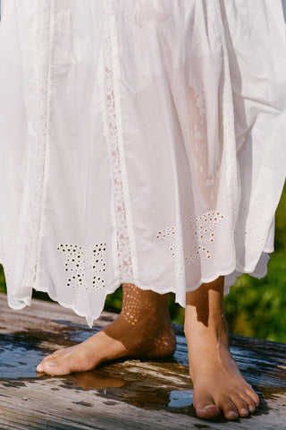 White skirt with lace details worn by a person standing on a wooden platform with water.