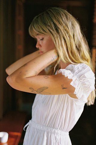 Woman in a white dress with tattoos on her arms, indoors.