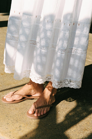 White lace-trimmed dress with brown sandals on a concrete surface