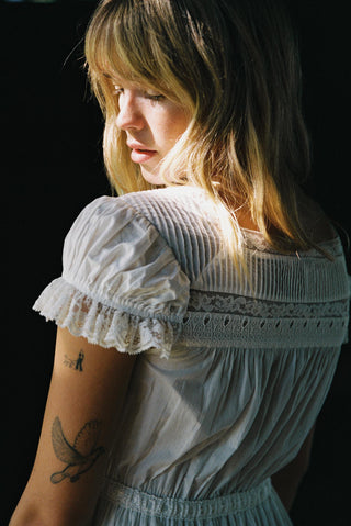 Woman wearing a light blue dress with lace details against a dark background