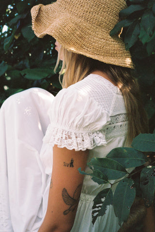 Person wearing a white dress and straw hat sitting among green leaves
