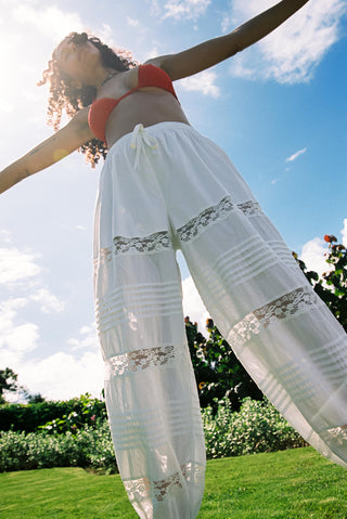 Woman in a red top and white pants standing on grass with a blue sky and clouds in the background