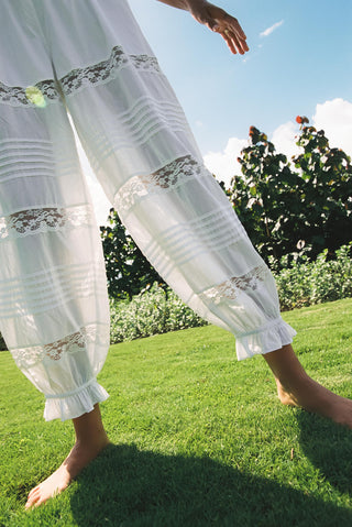 White lace-trimmed pants on a person standing on grass with a blue sky and trees in the background