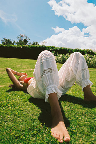 Person lying on grass wearing white pants with floral patterns
