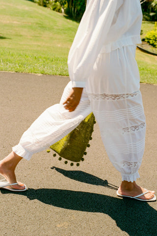 Person wearing white pants walking on a paved path with grass and trees in the background