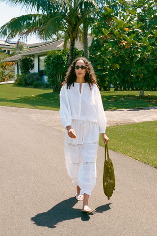 Woman in a white outfit walking on a road with greenery in the background