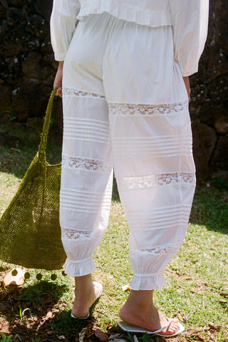 Person wearing white lace-trimmed pants holding a green bag outdoors.