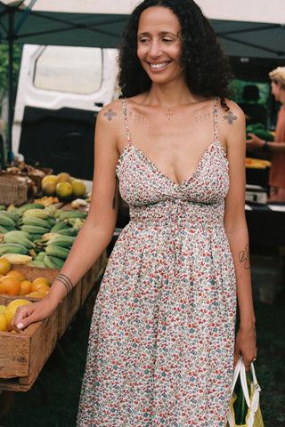 Woman in a floral dress standing at an outdoor market with produce in the background