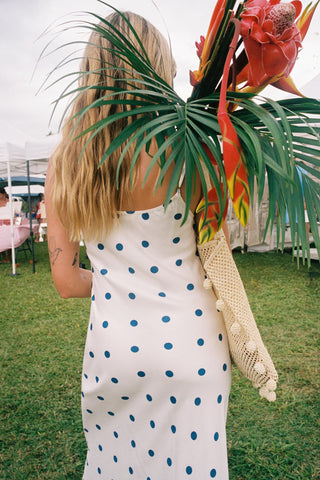 Person wearing a white dress with blue polka dots holding a bouquet of tropical flowers outdoors.
