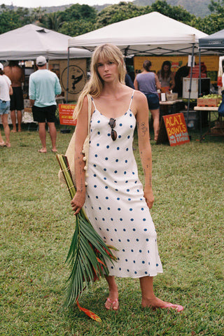 Woman in a polka dot dress holding a leafy green vegetable at an outdoor event.