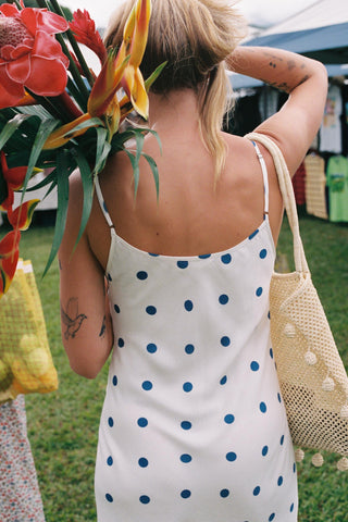 Woman in a polka dot dress holding flowers at an outdoor market.