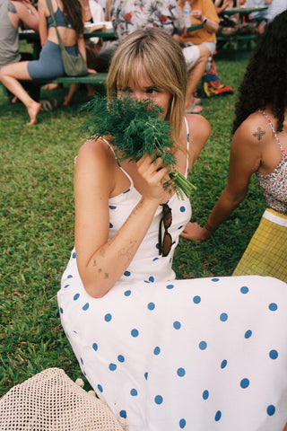 Woman in a polka dot dress holding greenery in a grassy outdoor setting