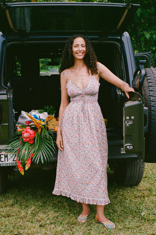 Woman in a floral dress standing behind a car with plants in the back seat