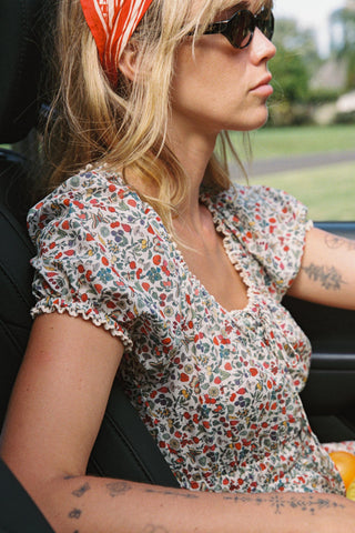 Woman sitting in a car wearing a floral dress and sunglasses