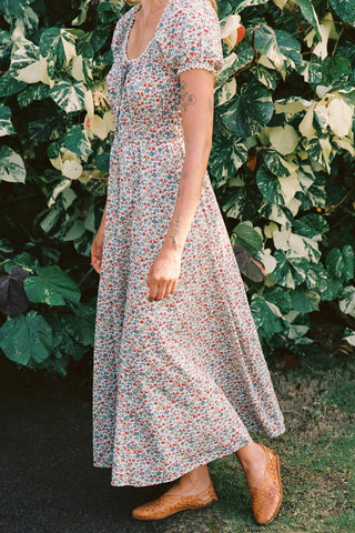 Woman wearing a floral dress standing in front of green foliage