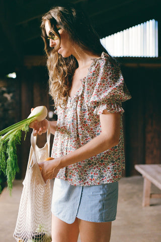 Woman in a floral blouse holding food and a market bag