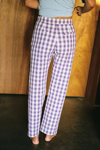 Person wearing purple checkered pants standing against a wooden wall.