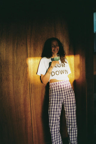 Person wearing a white t-shirt with text and checkered pants standing against a wooden wall.