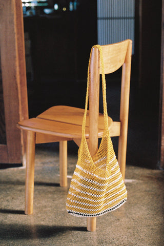 Yellow woven bag on a wooden chair with a dark background