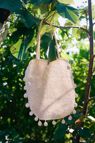 White woven bag with pom-poms hanging from a tree