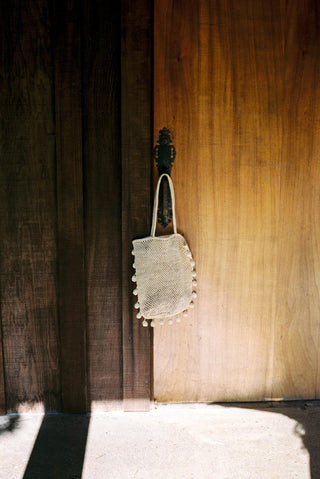 White mesh bag with decorative elements hanging on a wooden door.