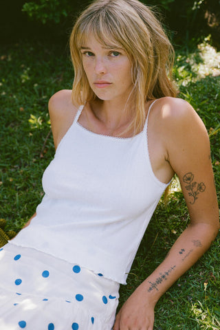 Woman in a white tank top and polka dot skirt sitting on grass