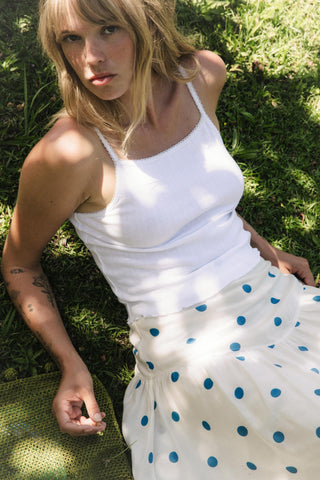 Woman wearing a white tank top and polka dot skirt sitting on grass