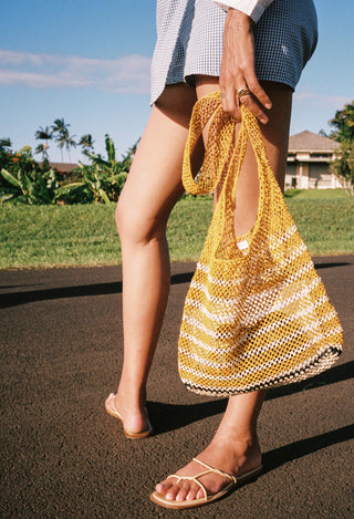 Person holding a yellow and white striped woven bag outdoors.