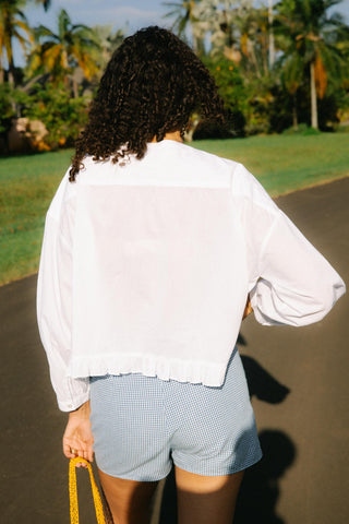 Person wearing a white shirt and checkered shorts walking on a path with greenery in the background