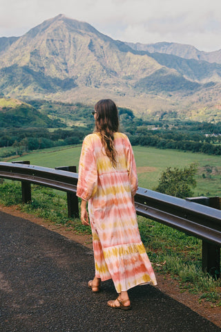 Woman in a tie-dye dress standing on a road with mountains in the background