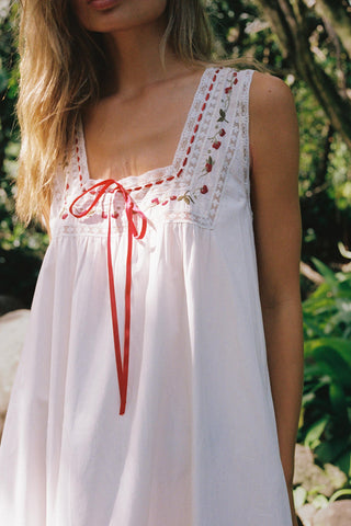 White dress with red embroidery and lace details worn by a woman outdoors.