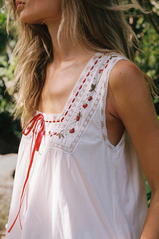 Woman wearing a white sleeveless dress with red embroidery in an outdoor setting