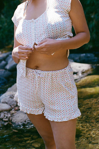 Person wearing a matching short and t-shirt set of a blue and red floral print on a white base standing by a stream